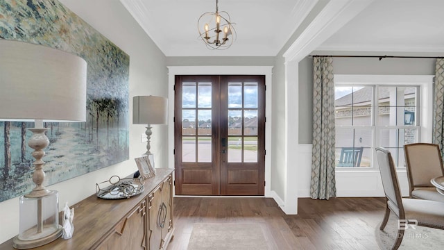foyer entrance featuring an inviting chandelier, hardwood / wood-style flooring, crown molding, wainscoting, and french doors