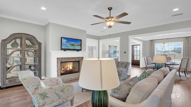 living area with visible vents, a brick fireplace, ornamental molding, wood finished floors, and ceiling fan with notable chandelier