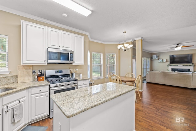 kitchen with decorative light fixtures, stainless steel appliances, a kitchen island, white cabinets, and ornamental molding