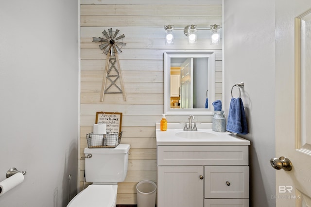 bathroom with toilet, wood walls, and vanity