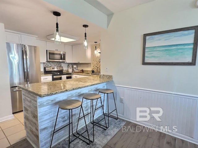 kitchen with appliances with stainless steel finishes, white cabinets, kitchen peninsula, a breakfast bar area, and pendant lighting