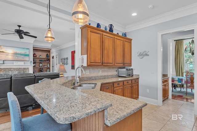 kitchen with brown cabinets, ceiling fan, a sink, a breakfast bar area, and a peninsula