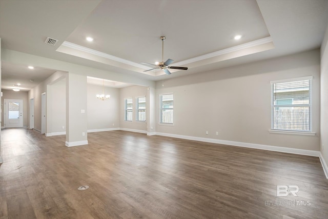 unfurnished living room featuring ceiling fan with notable chandelier, a tray ceiling, dark hardwood / wood-style floors, and crown molding