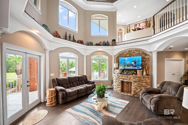 living area with decorative columns, a high ceiling, healthy amount of natural light, hardwood / wood-style floors, and crown molding