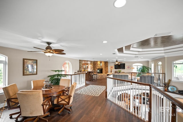 dining space featuring a ceiling fan, wood finished floors, a fireplace, a tray ceiling, and crown molding