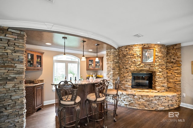 indoor bar featuring dark wood finished floors, a stone fireplace, crown molding, baseboards, and hanging light fixtures