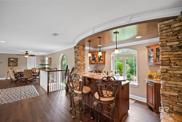 indoor wet bar featuring dark wood-type flooring, baseboards, ceiling fan, decorative light fixtures, and ornamental molding