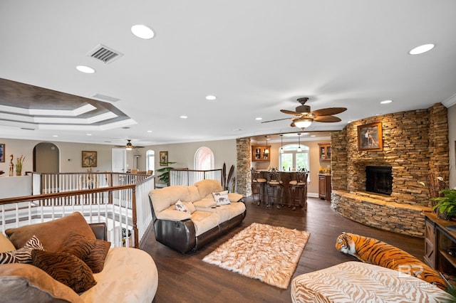 living area with ceiling fan, crown molding, recessed lighting, dark wood-style floors, and a stone fireplace