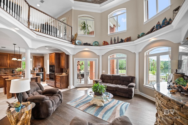 living room with ornate columns, french doors, a towering ceiling, crown molding, and light wood-style flooring