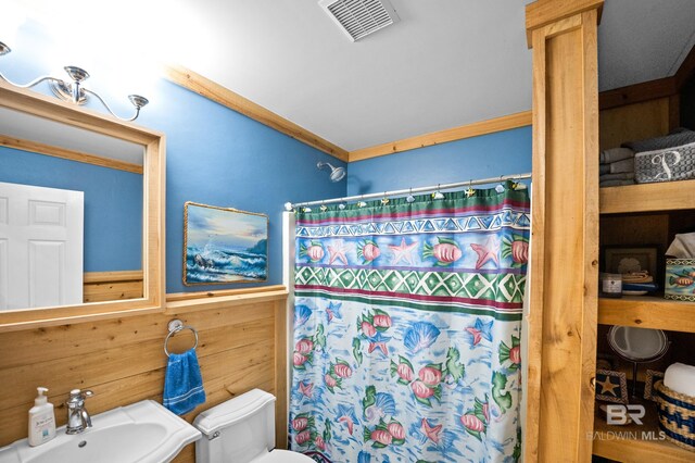 bathroom featuring a sink, toilet, a shower with shower curtain, wood walls, and wainscoting