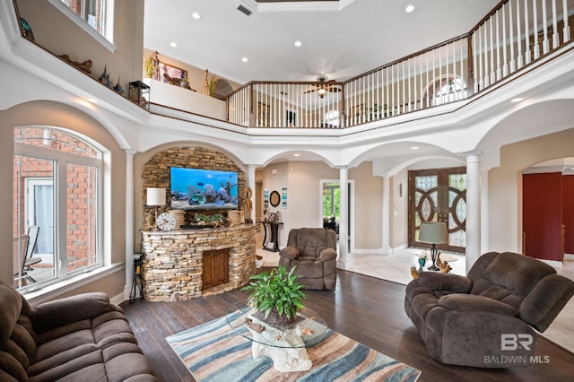 living area featuring decorative columns, a high ceiling, recessed lighting, a stone fireplace, and baseboards