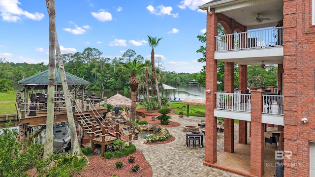 view of yard with a balcony, a water view, a ceiling fan, and a patio