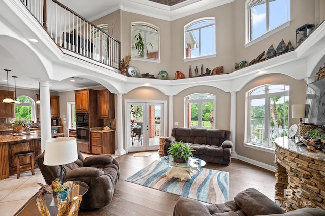 living area featuring decorative columns, healthy amount of natural light, a high ceiling, light wood-style flooring, and crown molding