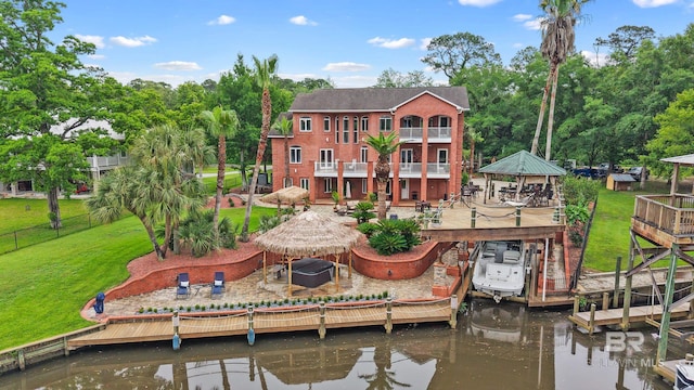 back of property featuring a gazebo, a deck with water view, boat lift, and view of wooded area