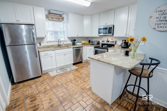 kitchen with light stone countertops, sink, kitchen peninsula, white cabinets, and appliances with stainless steel finishes