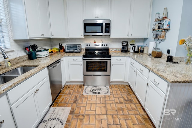 kitchen with light stone countertops, white cabinetry, sink, stainless steel appliances, and decorative backsplash