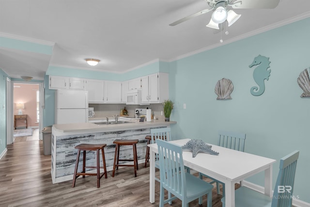 kitchen featuring white cabinetry, hardwood / wood-style flooring, ornamental molding, kitchen peninsula, and white appliances