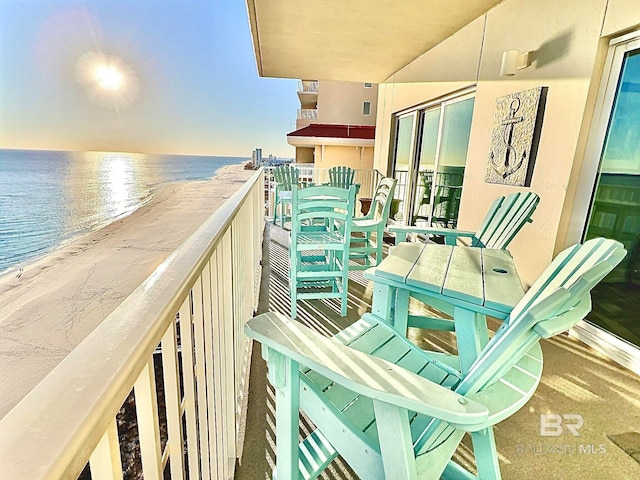 balcony at dusk with a water view and a view of the beach