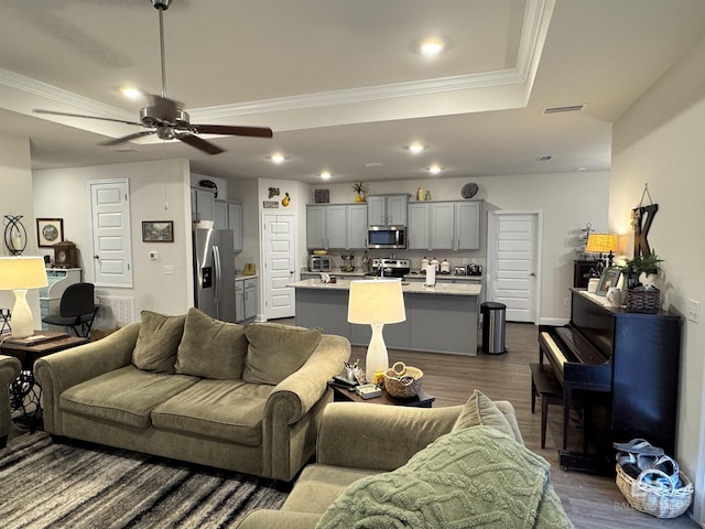 living room featuring ceiling fan, wood-type flooring, ornamental molding, and a raised ceiling