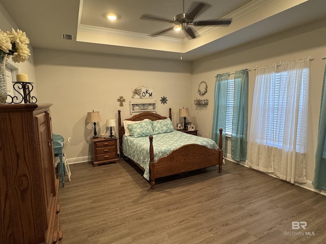 bedroom featuring ceiling fan, crown molding, dark wood-type flooring, and a tray ceiling