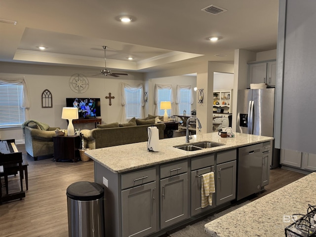 kitchen with sink, gray cabinetry, a tray ceiling, a center island with sink, and stainless steel appliances