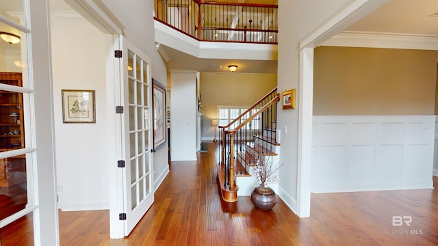 foyer with hardwood / wood-style floors, a towering ceiling, ornamental molding, and french doors