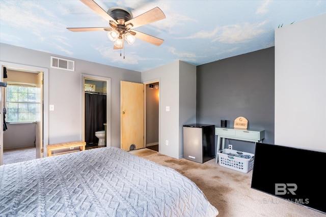 bedroom featuring light carpet, ensuite bathroom, stainless steel refrigerator, and ceiling fan