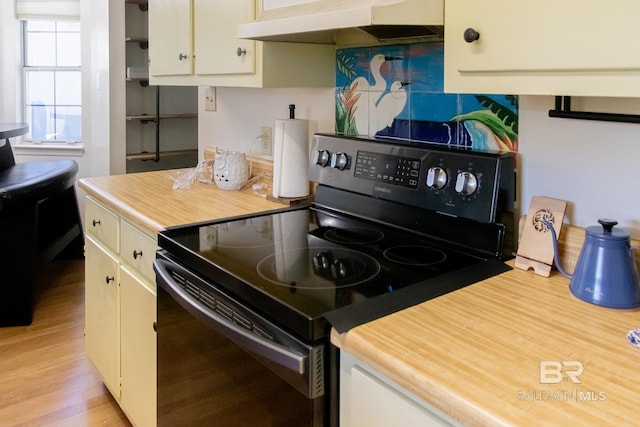 kitchen featuring light hardwood / wood-style floors, black range with electric stovetop, and cream cabinetry