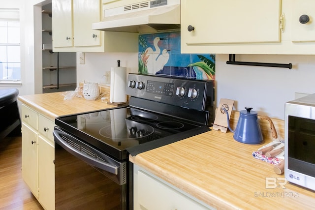 kitchen featuring black electric range, light hardwood / wood-style flooring, and backsplash