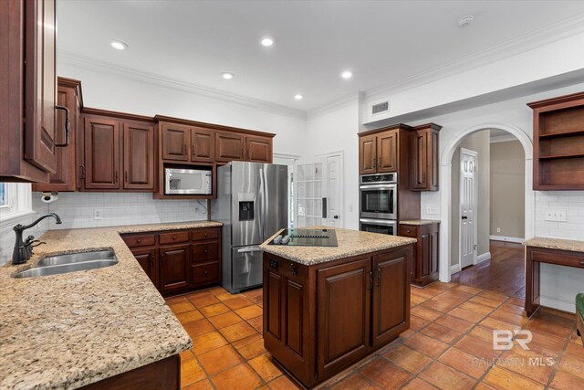 kitchen with sink, a kitchen island, appliances with stainless steel finishes, crown molding, and light stone countertops