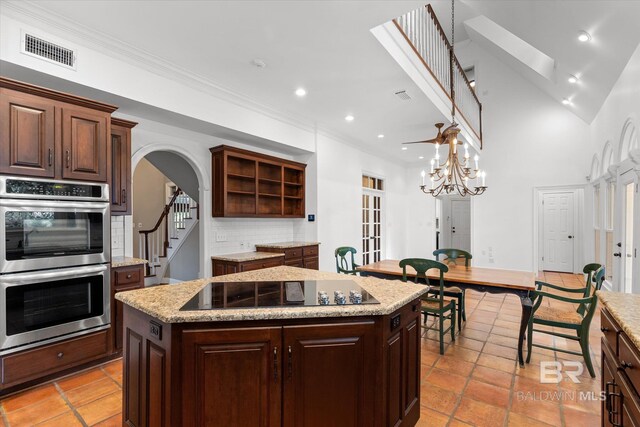 kitchen featuring black electric cooktop, tasteful backsplash, stainless steel double oven, a center island, and a skylight