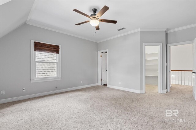 unfurnished bedroom featuring vaulted ceiling, crown molding, ceiling fan, a walk in closet, and light carpet