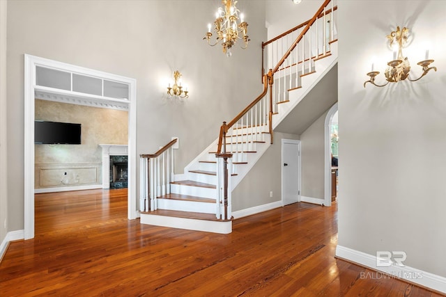 stairs featuring a notable chandelier, a high ceiling, hardwood / wood-style flooring, and a fireplace