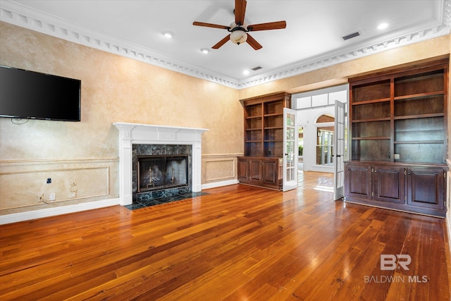 unfurnished living room with dark hardwood / wood-style floors, built in shelves, a fireplace, crown molding, and ceiling fan