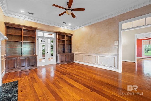 unfurnished living room featuring wood-type flooring, built in shelves, crown molding, ceiling fan, and french doors