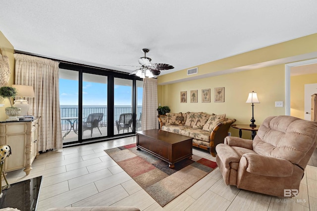 living area featuring a water view, floor to ceiling windows, visible vents, and a ceiling fan