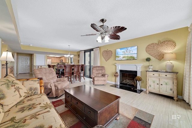 living area with a textured ceiling, ceiling fan with notable chandelier, baseboards, and a fireplace with raised hearth