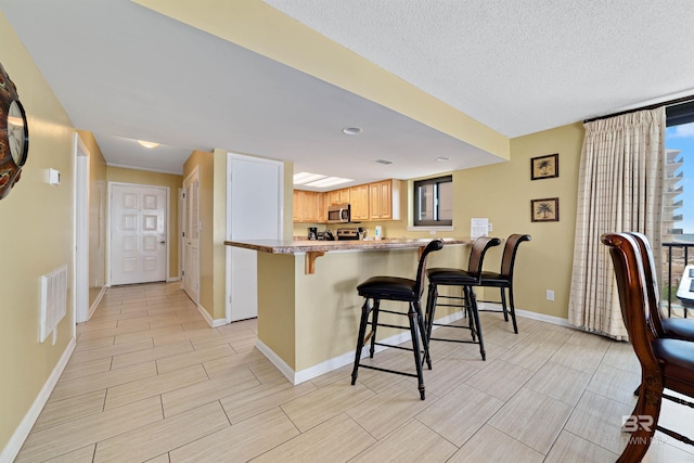 kitchen featuring stainless steel microwave, a peninsula, a breakfast bar, visible vents, and baseboards