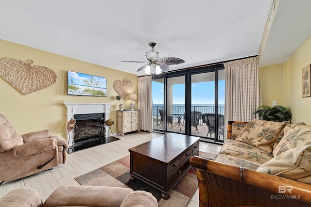 living area featuring a fireplace with flush hearth, a textured ceiling, and a ceiling fan