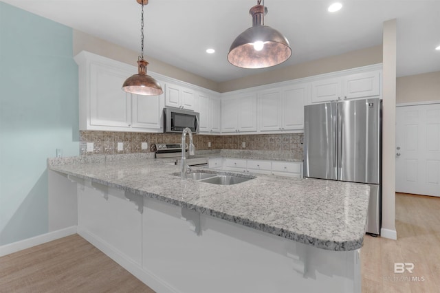 kitchen with appliances with stainless steel finishes, white cabinetry, decorative light fixtures, and kitchen peninsula