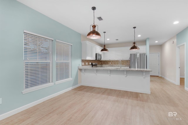 kitchen featuring kitchen peninsula, hanging light fixtures, tasteful backsplash, white cabinetry, and appliances with stainless steel finishes