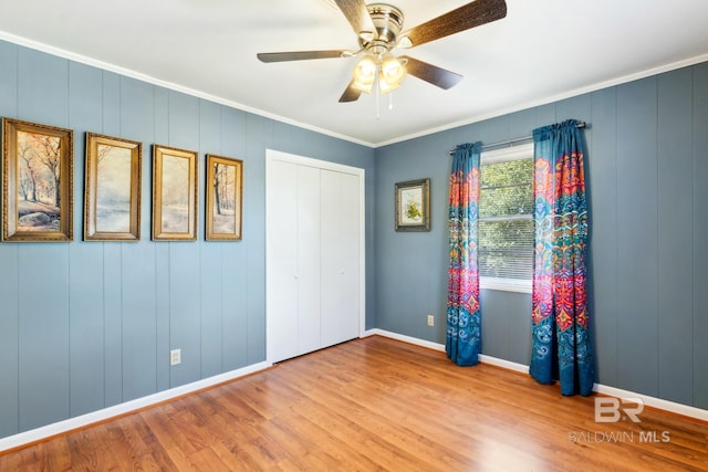 unfurnished bedroom with wood finished floors, a closet, ceiling fan, baseboards, and ornamental molding