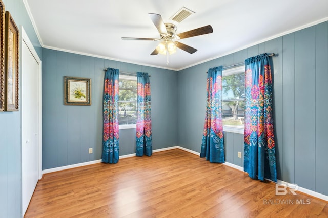 empty room featuring wood finished floors, visible vents, crown molding, baseboards, and ceiling fan