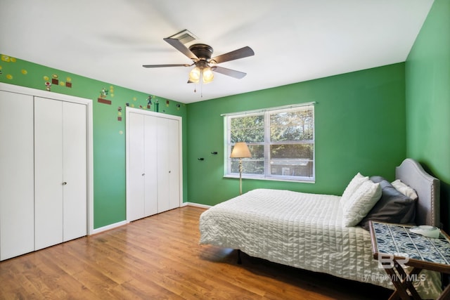 bedroom featuring baseboards, multiple closets, wood finished floors, and ceiling fan