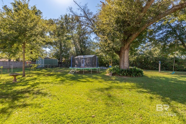 view of yard featuring an outdoor structure, fence, a shed, and a trampoline