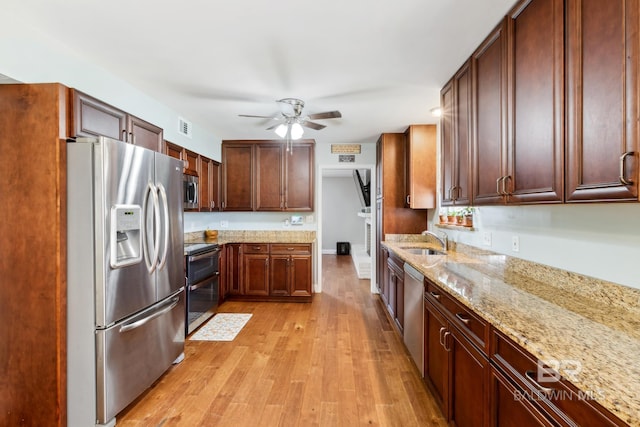 kitchen featuring light stone counters, a sink, light wood-type flooring, ceiling fan, and stainless steel appliances