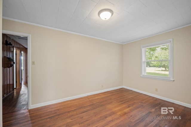 empty room featuring wood finished floors, ornamental molding, and baseboards