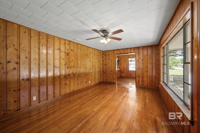 unfurnished room featuring wood finished floors, healthy amount of natural light, ceiling fan, wood walls, and baseboards