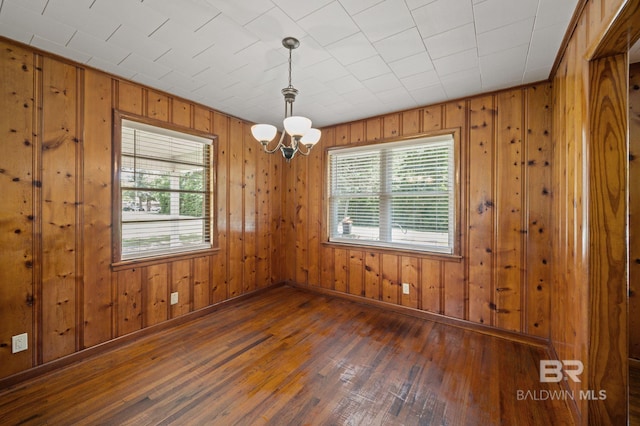 spare room with wood-type flooring, a chandelier, wooden walls, and baseboards