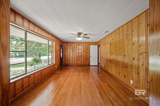unfurnished room featuring light wood-style floors, wooden walls, and ceiling fan